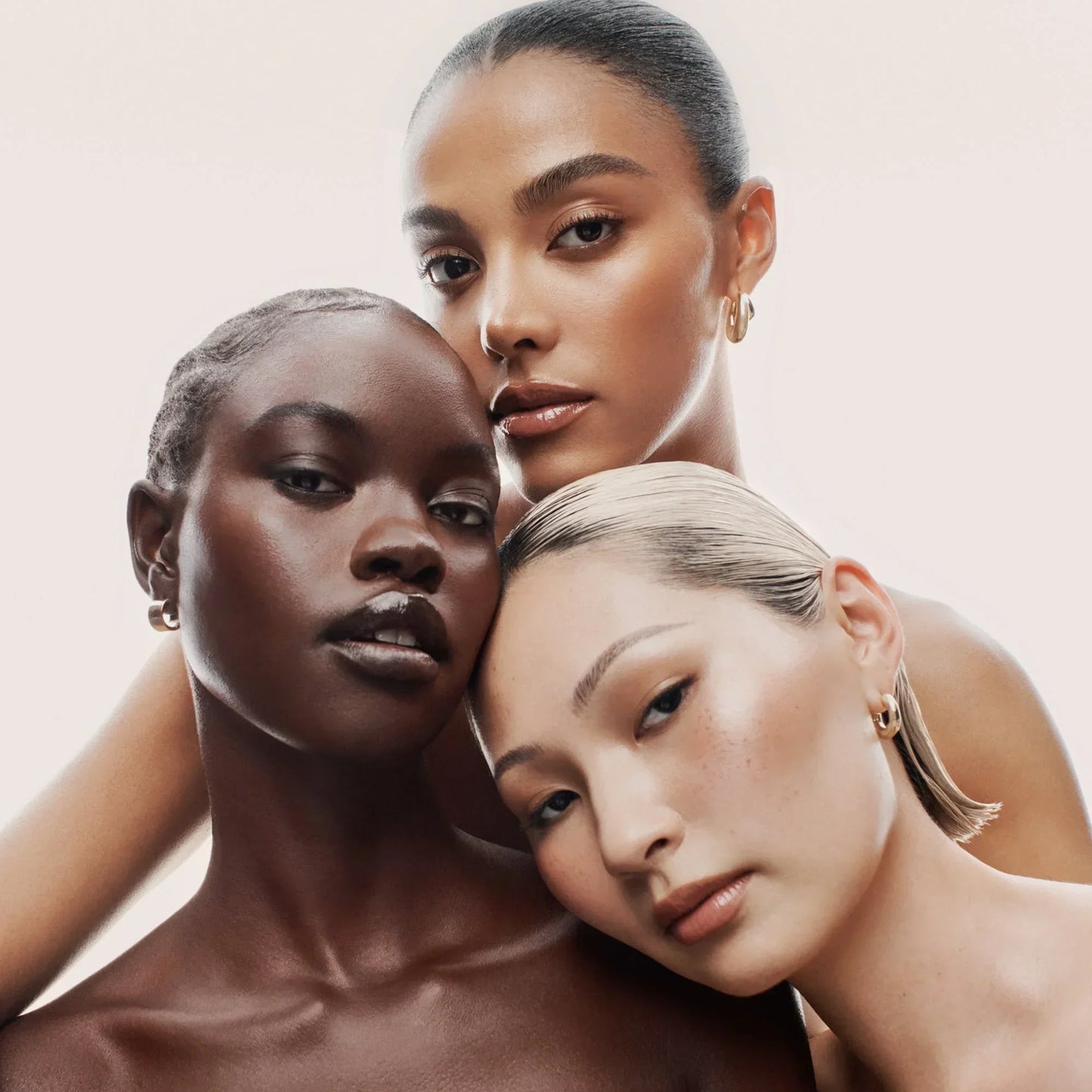 Three women with radiant, flawless skin in diverse tones, featuring dewy, luminous makeup.
