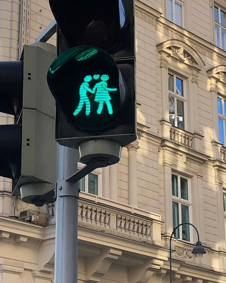 Green pedestrian traffic light with two figures holding hands and heart symbols, city background.