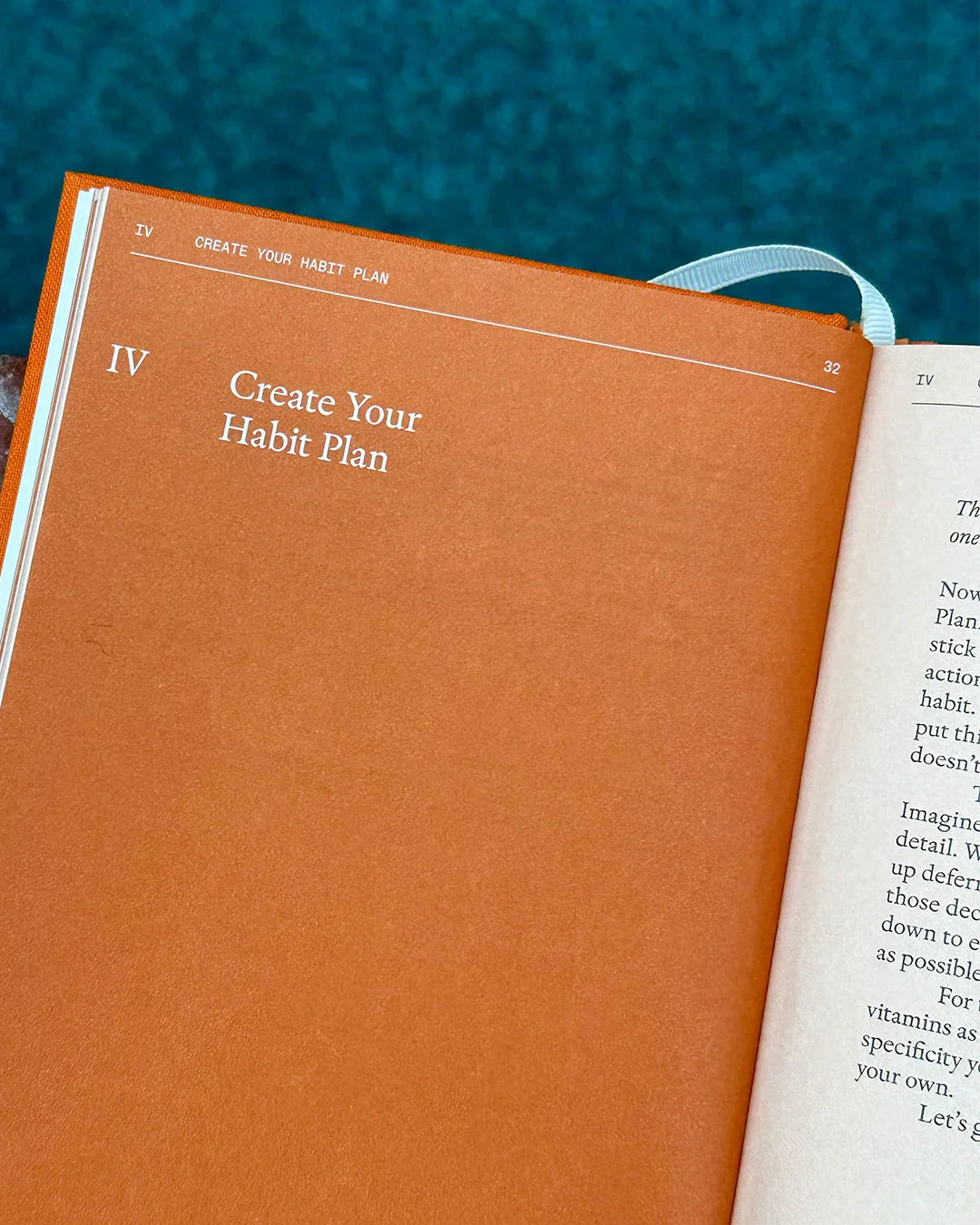 Open planner with a matte orange textured page titled 'Create Your Habit Plan' next to white page, on a blue fabric background.