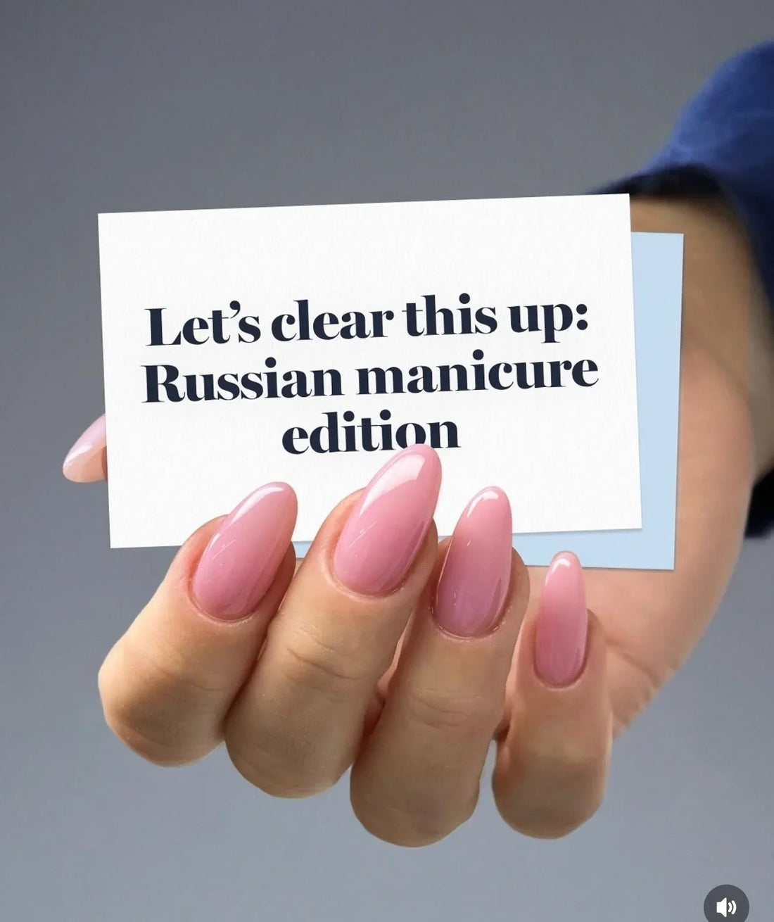 Hand with glossy, almond-shaped pink nails holding a card about Russian manicure edition.
