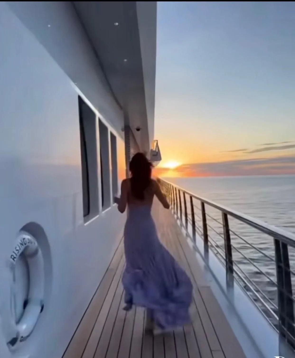 Woman in flowing lavender dress walking on yacht deck at sunset, luxury ocean scenery