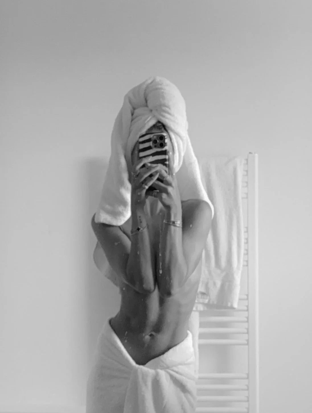 Chic black and white mirror selfie of woman in plush white towel with smooth, radiant skin.