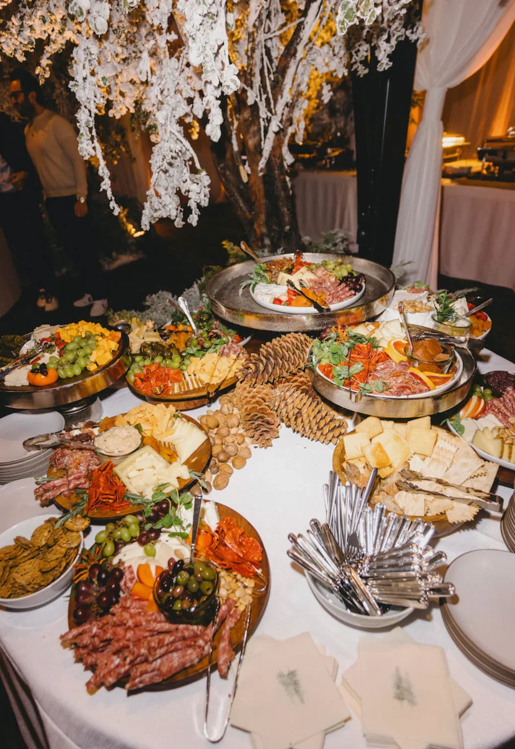 Elegant charcuterie and cheese platter with fresh grapes, olives, and assorted crackers, set on a white table beneath frosted winter branches.