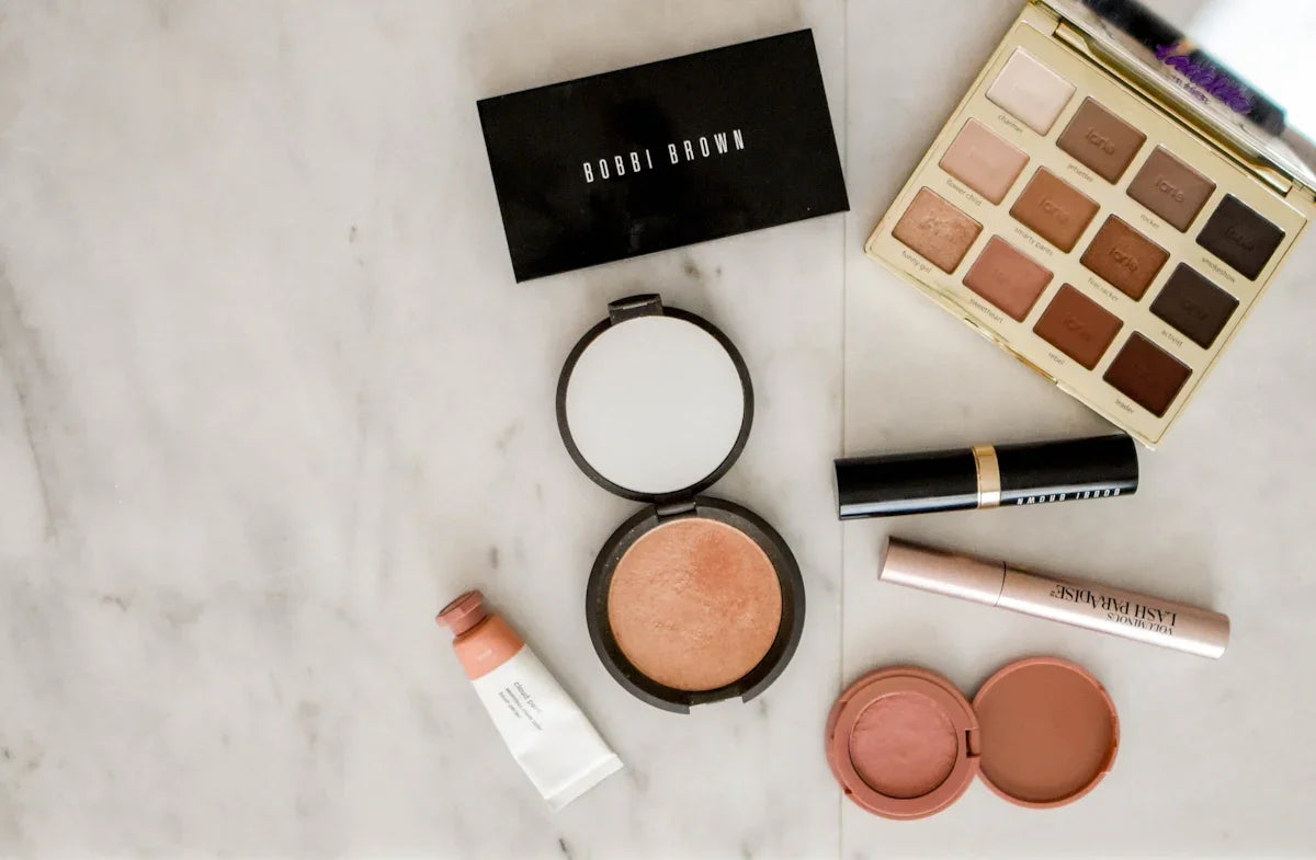 Luxury neutral eyeshadow palette, creamy blush, dewy highlighter, and volumizing mascara on marble