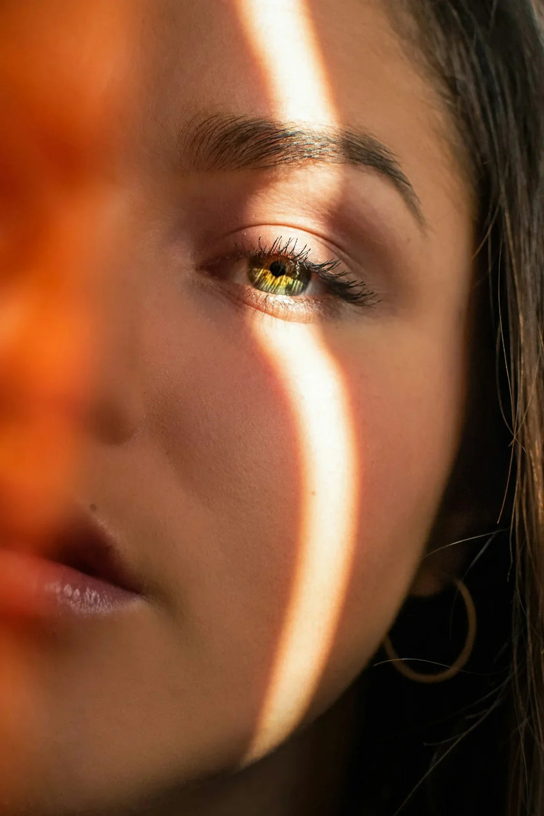 Close-up of a woman's green eye and dewy skin in warm natural sunlight, soft focus, luxury beauty