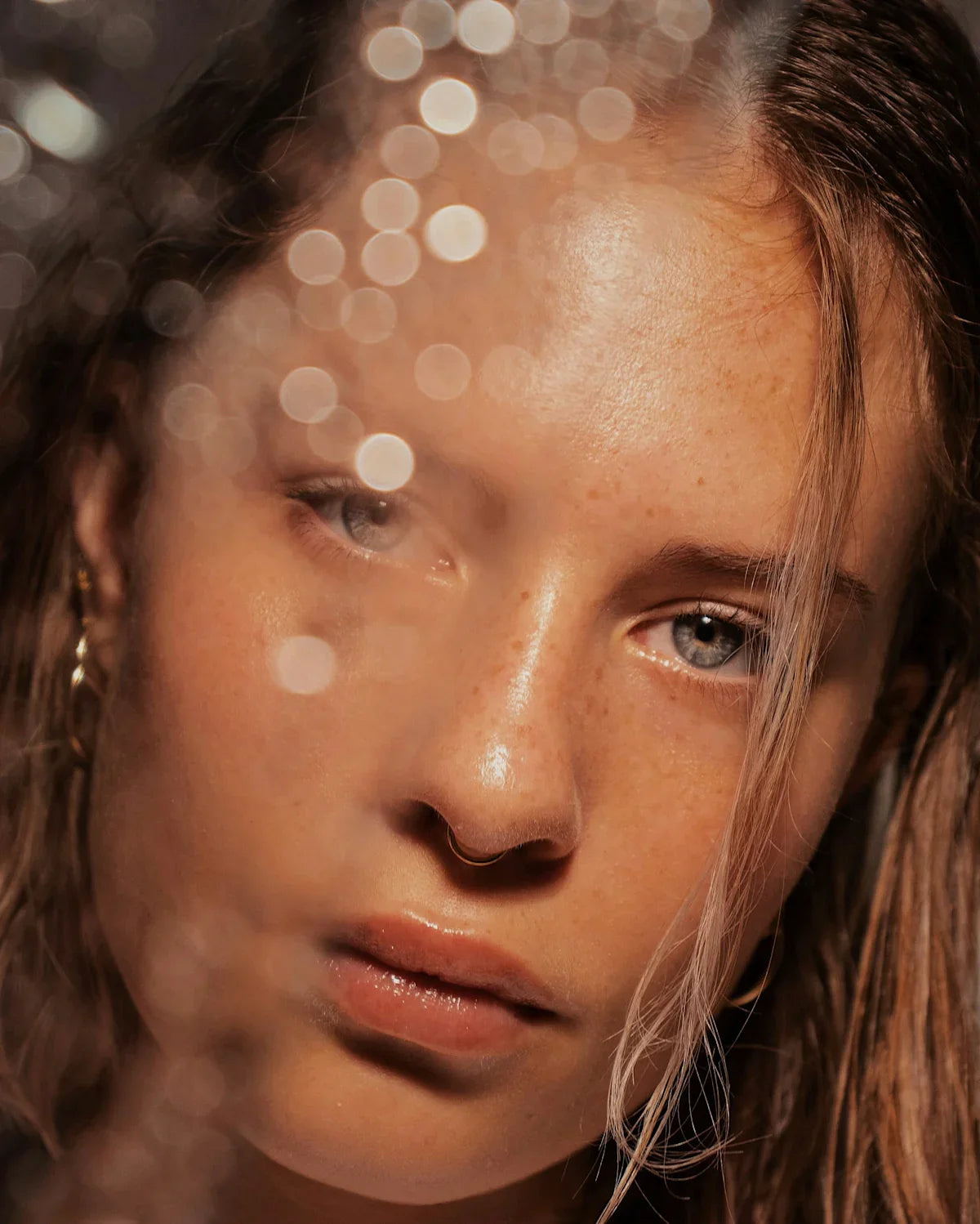 Close-up of woman with dewy, glowing skin, natural freckles, glossy lips, and soft lighting effects.