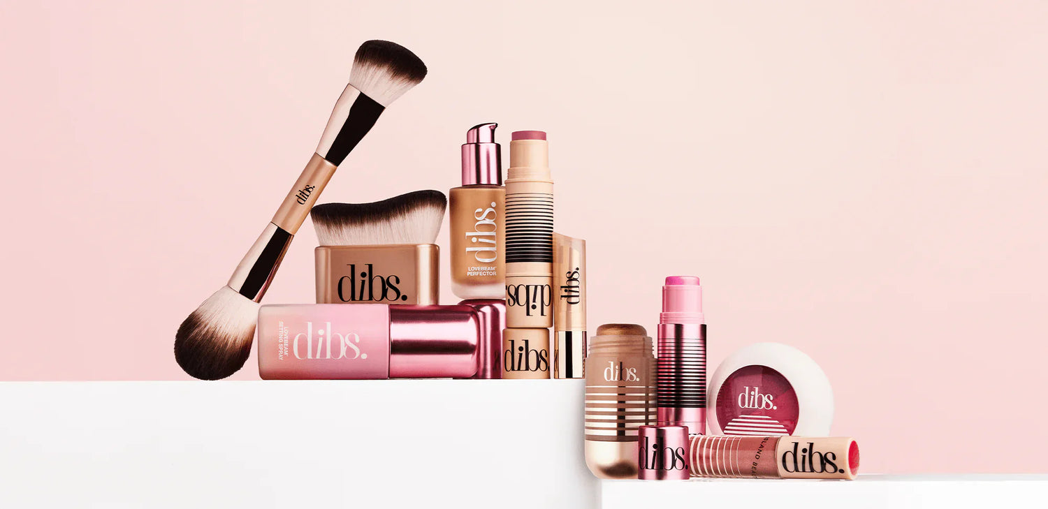 Luxurious makeup collection with gold, rose, and nude tones, featuring creamy sticks, powder blush, silky brushes, and pink highlights on a soft blush background.