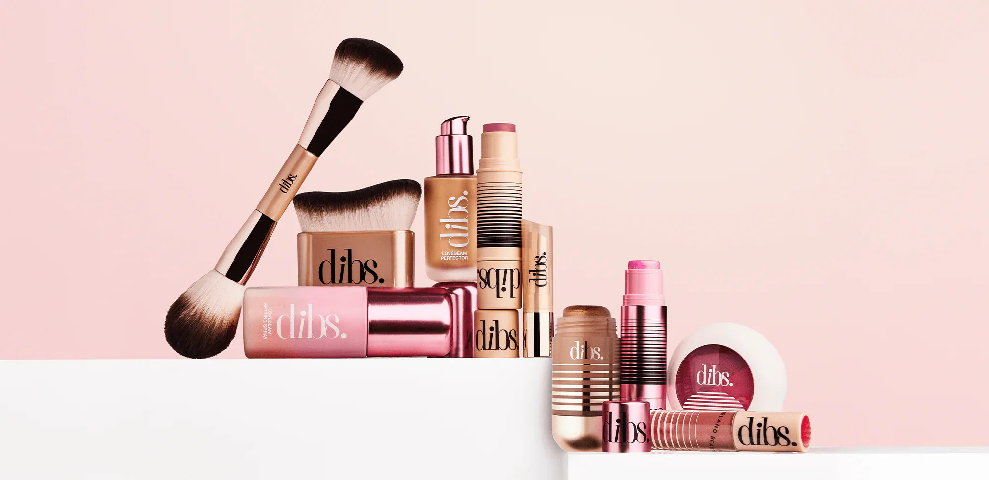 Luxurious makeup collection with gold, rose, and nude tones, featuring creamy sticks, powder blush, silky brushes, and pink highlights on a soft blush background.