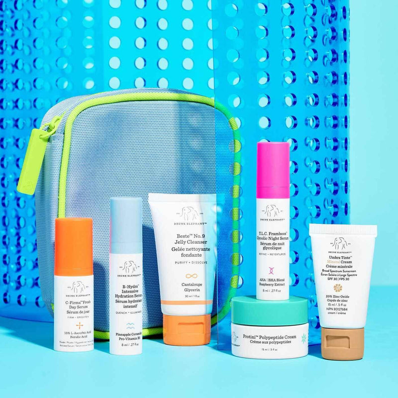 Drunk Elephant skincare travel set with colorful bottles and pouch on a blue background