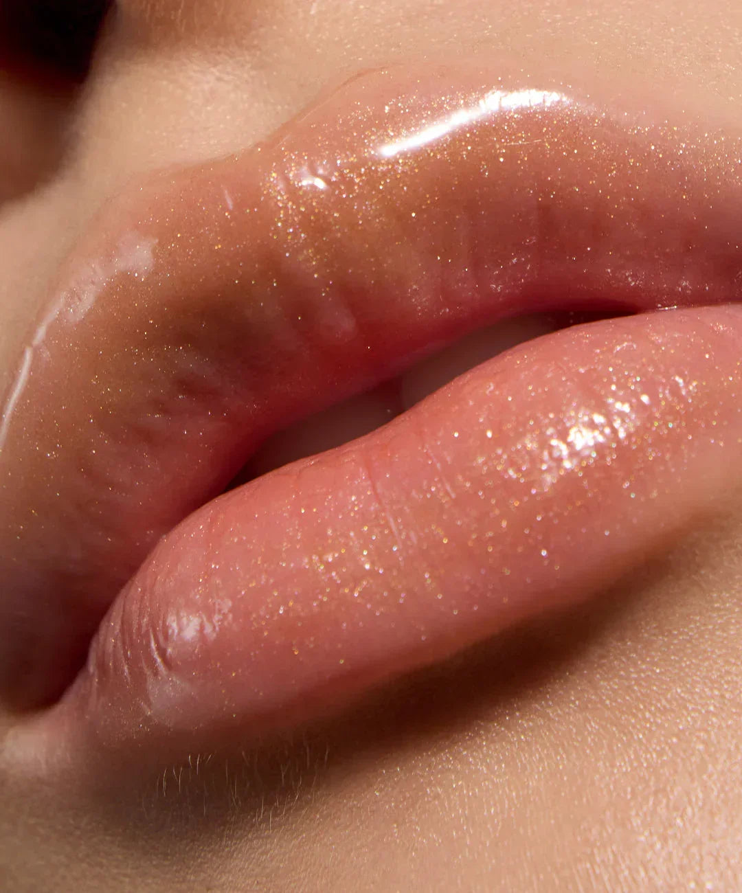 Close-up of lips with glossy, nude pink lip gloss and shimmering gold flecks