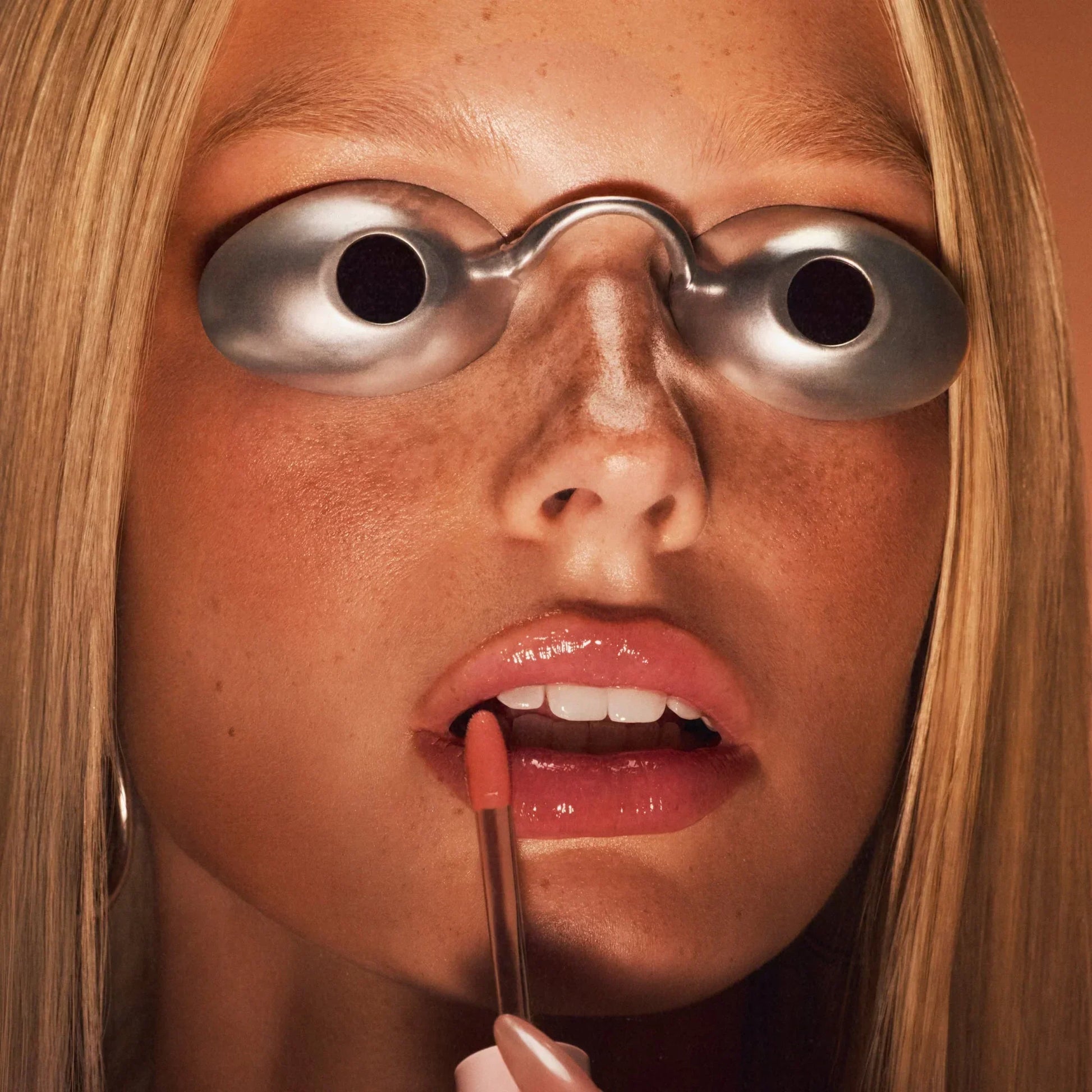 Model applying lip oil with goggles on.