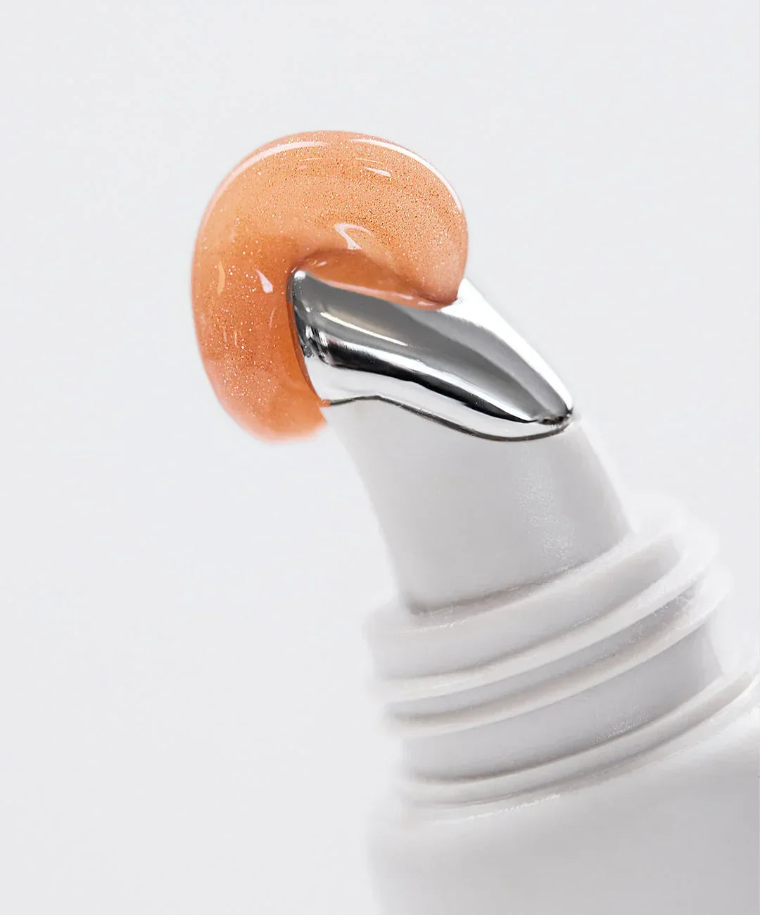 Shimmery peach gel with dewy finish on a sleek silver applicator, luxury skincare texture