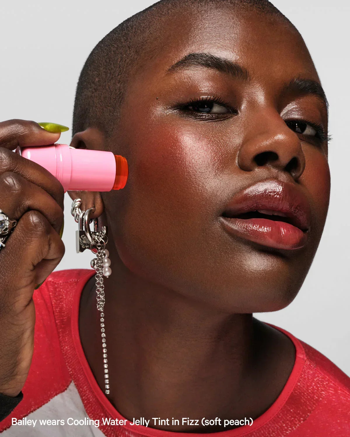 Person applies Cooling Water Jelly Tint Fizz to cheek, glossy lips, statement earrings