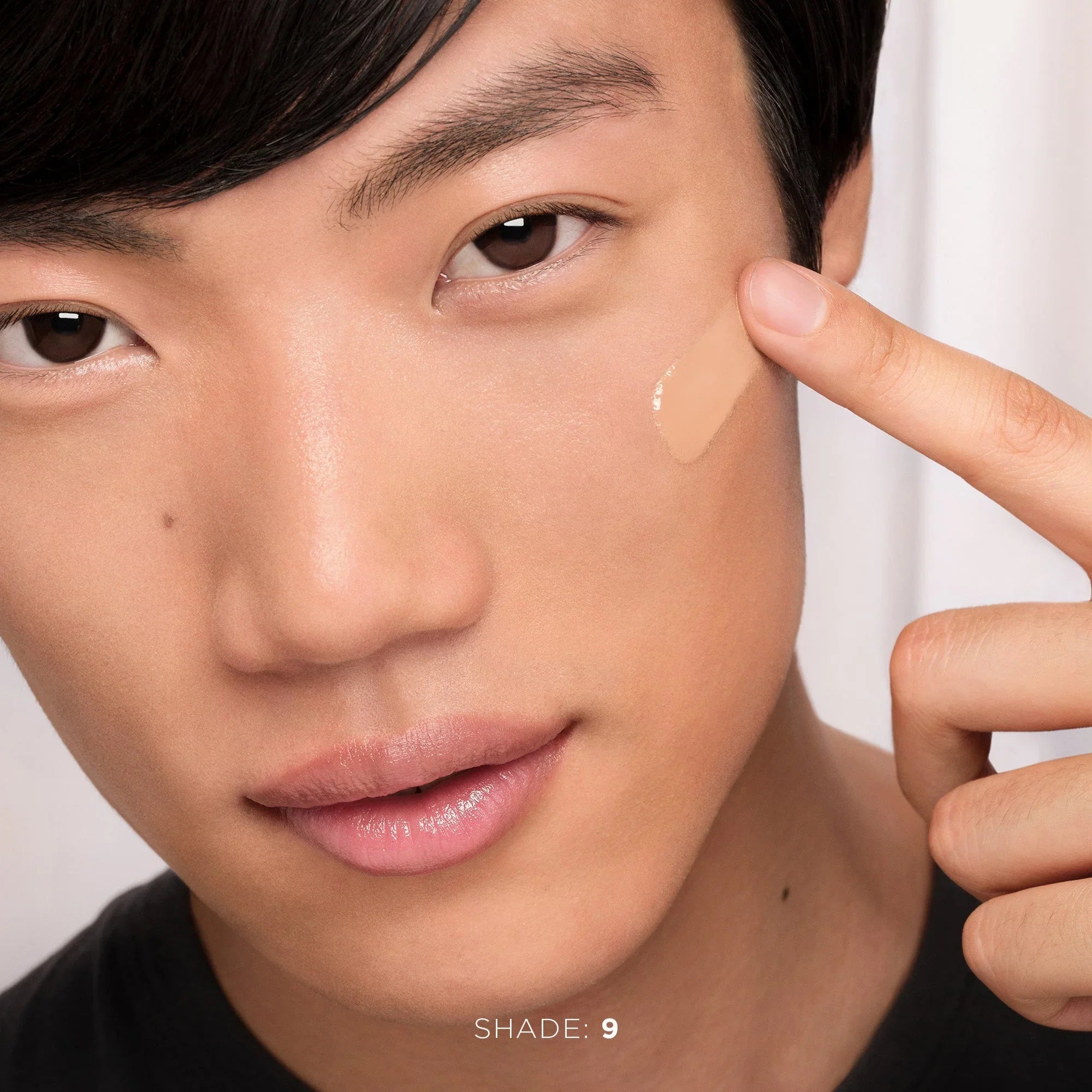 Model applying dewy beige foundation shade 9 to cheek, glowing skin, Wylde Grey beauty