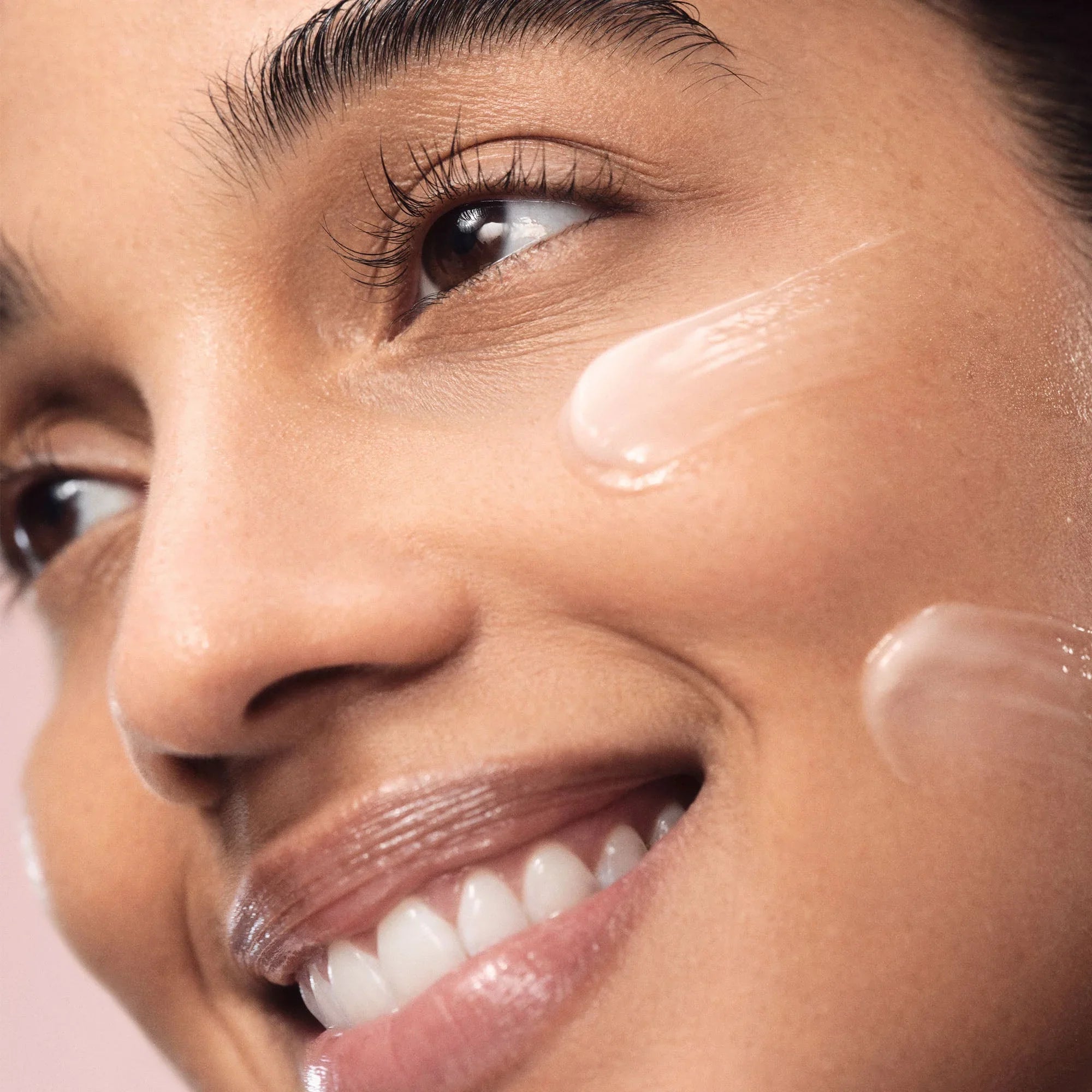 Close-up of model with glowing skin applying dewy, creamy moisturizer on cheek, Wylde Grey