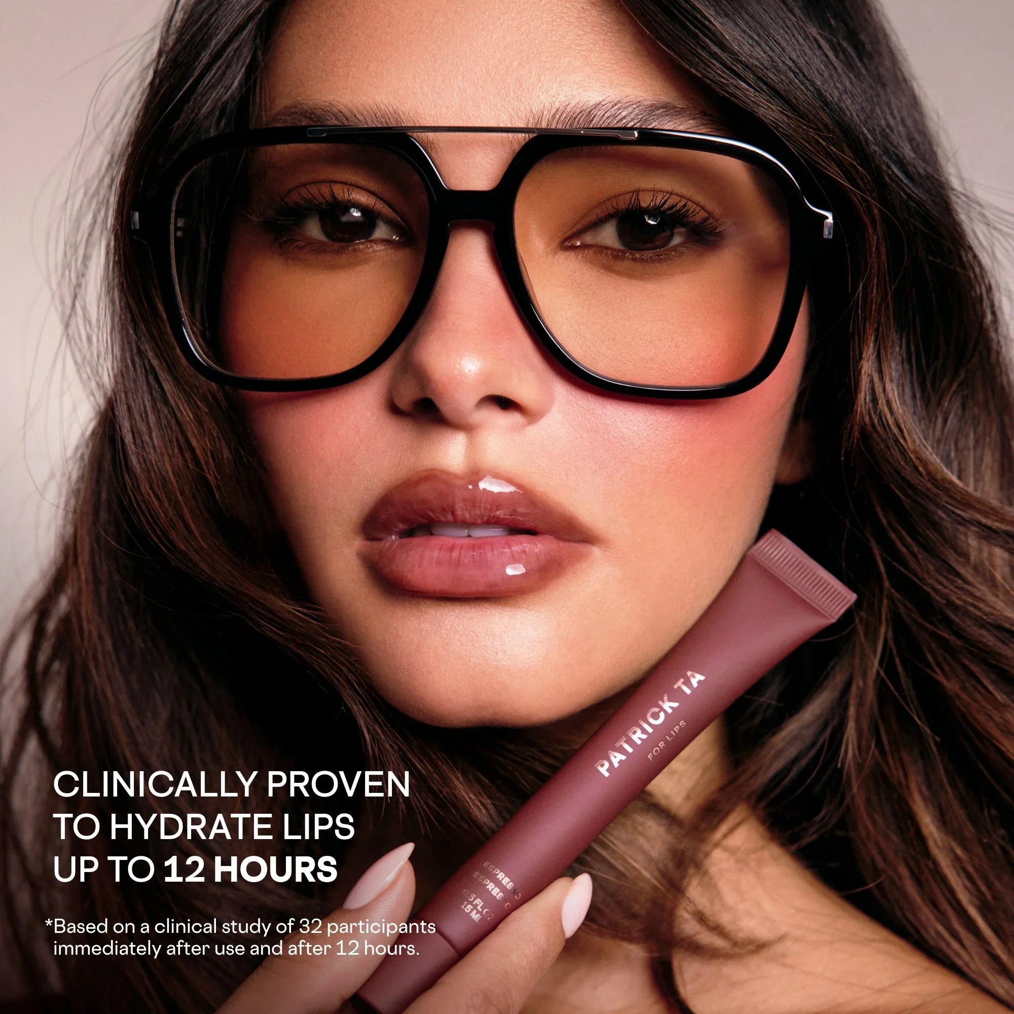 Model with glossy, hydrated lips, brown sunglasses, holding Patrick Ta lip balm, luxury skincare