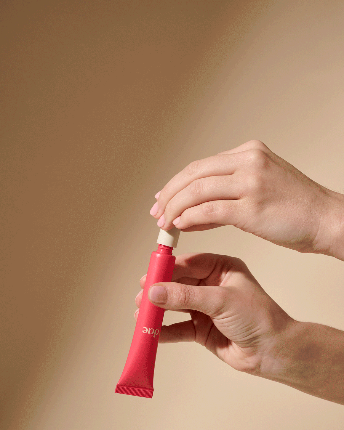 Luxurious red 3-in-1 beauty wand with creamy texture, held in elegant hands on beige backdrop