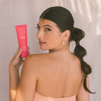 Woman with sleek bubble ponytail holding Dae pink beauty tube, glowing skin, soft neutral backdrop