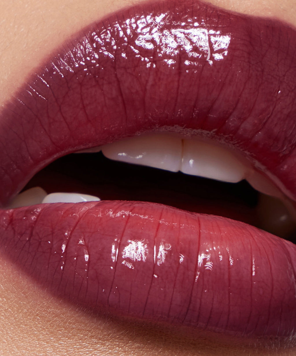 Close-up of glossy dark plum lipstick on parted lips, showing smooth, hydrated finish