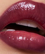 Close-up of glossy dark plum lipstick on parted lips, showing smooth, hydrated finish
