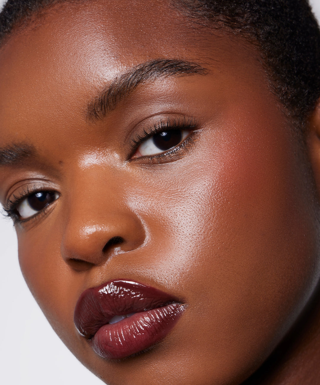 Close-up of woman with dewy skin, natural makeup, and glossy dark plum lipstick