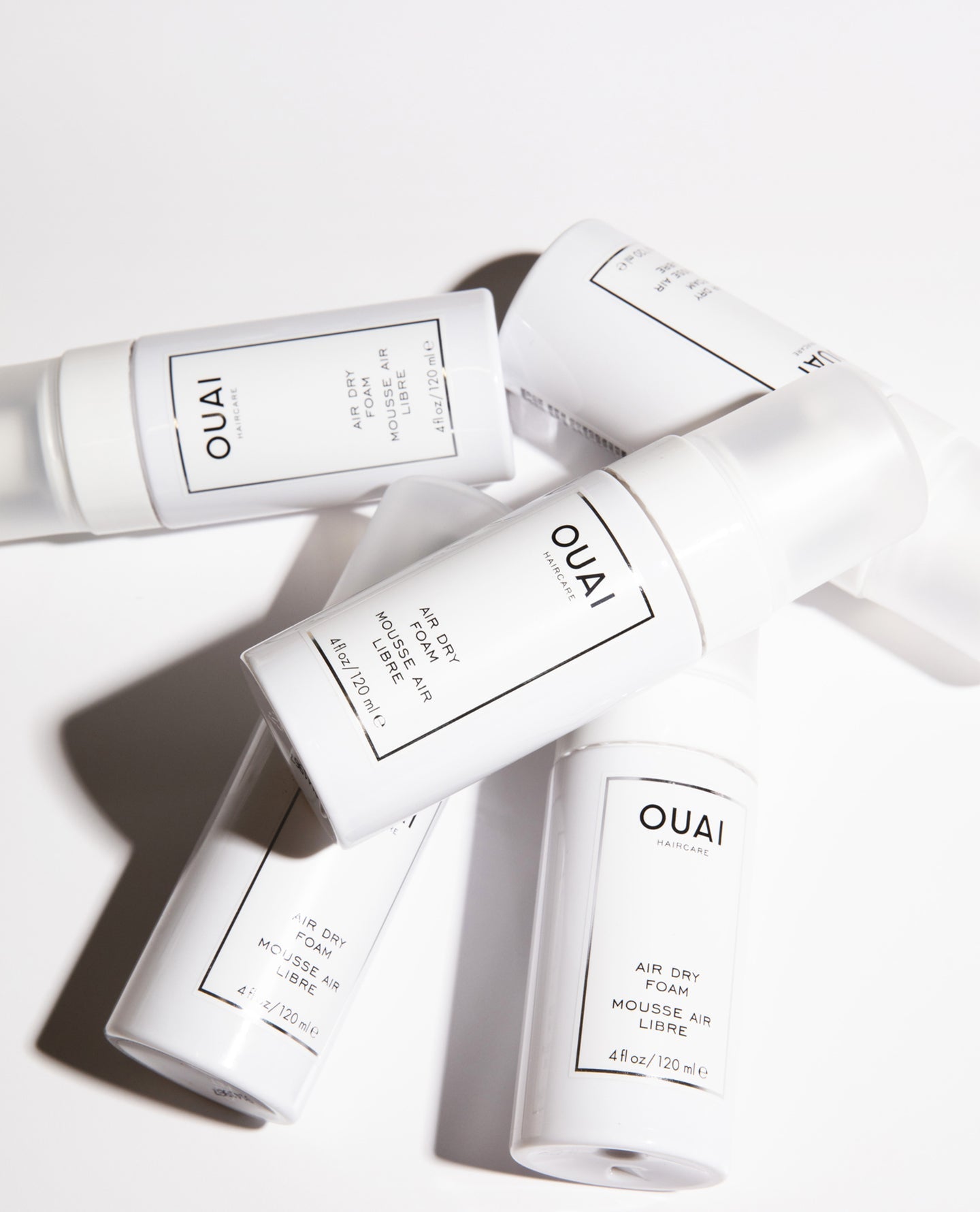 OUAI Haircare Air Dry Foam 4fl oz cans scattered on white surface.