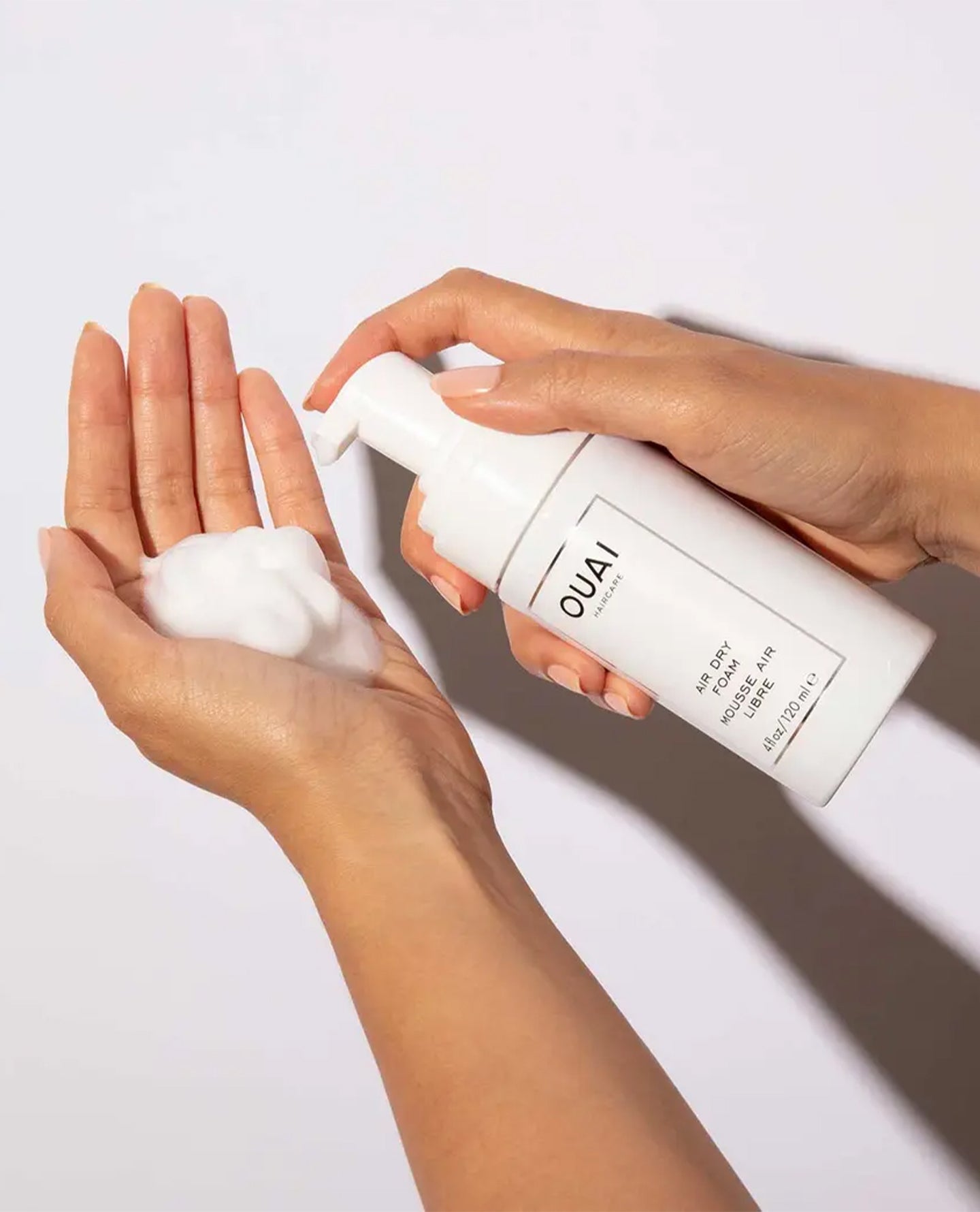 OUAI Air Dry Foam being dispensed onto open palm from white pump bottle.
