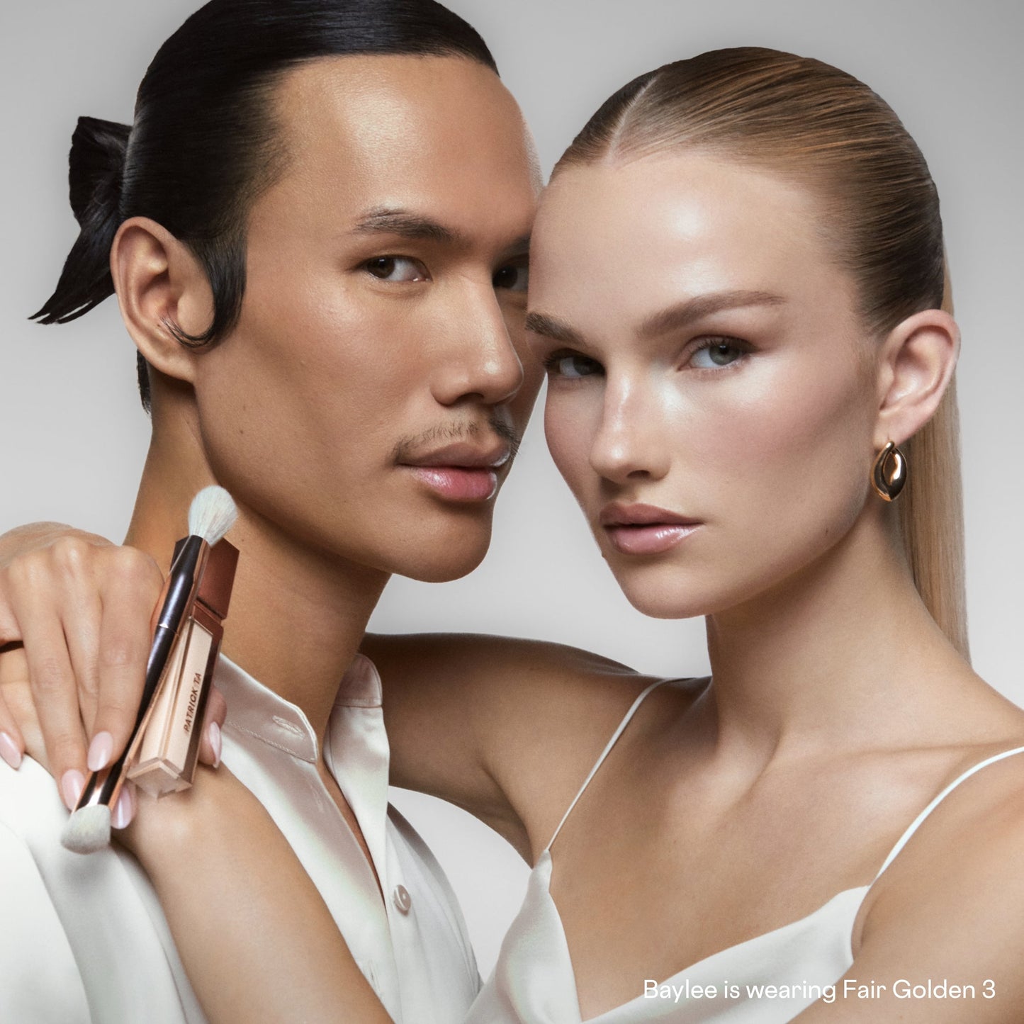 Two models with flawless, dewy skin wearing creamy concealer shades, one holding a makeup brush.