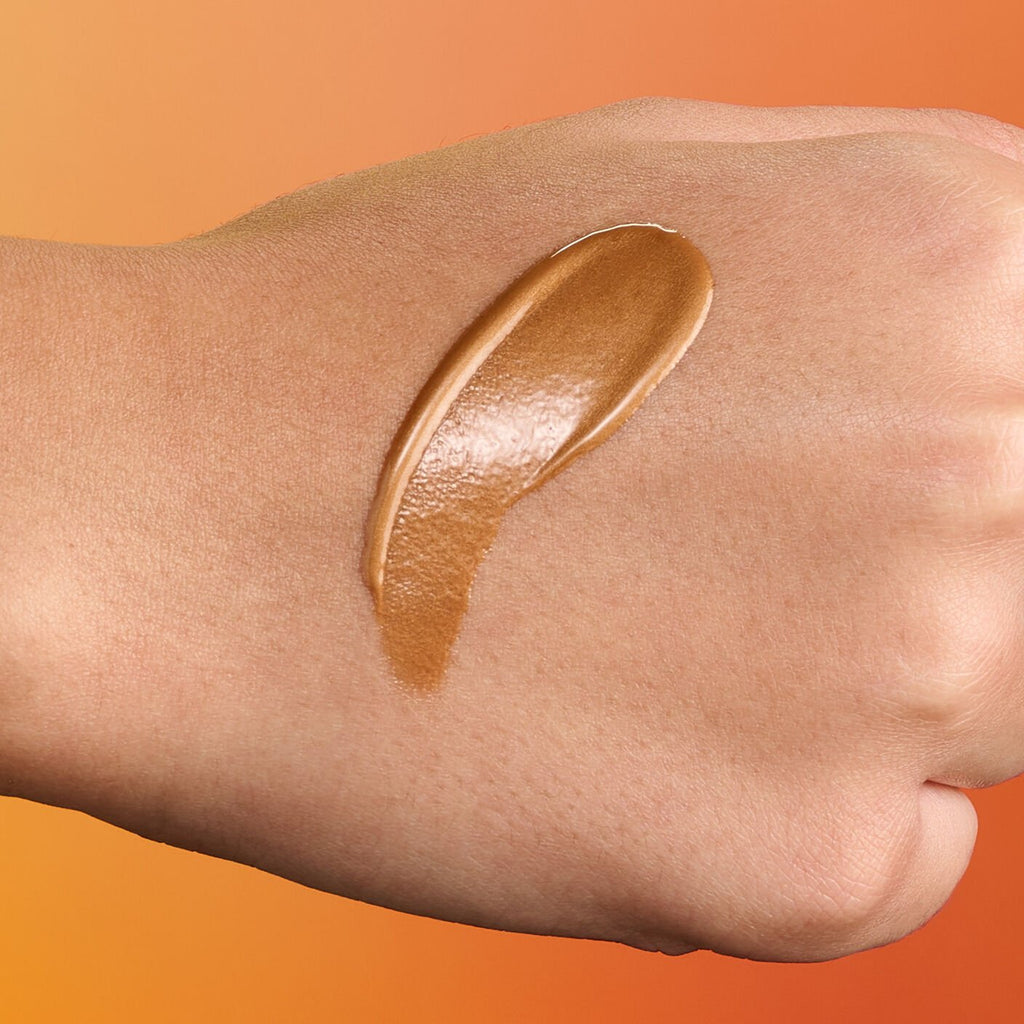 Bronzing serum swatch on hand with orange gradient background