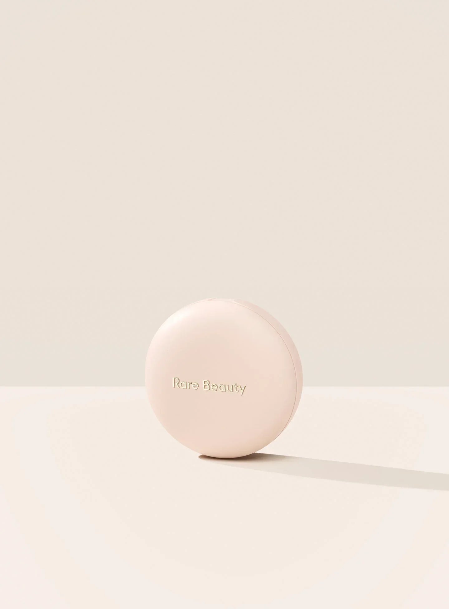 | The exterior of Rare Beauty's Soft Pinch Luminous Powder Blush is displayed with its simple neutral pink case and "Rare Beauty" etched on the outside.
