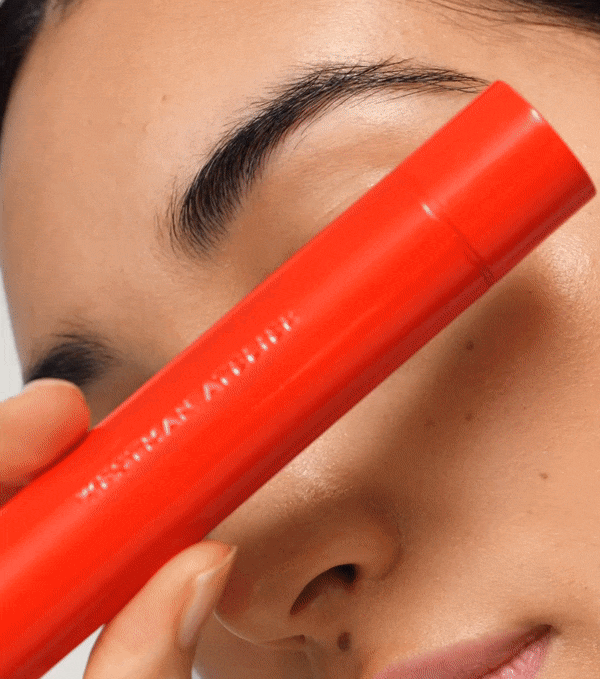 Close-up of a model with flawless skin holding a luxe red mascara tube by Wylde Grey.