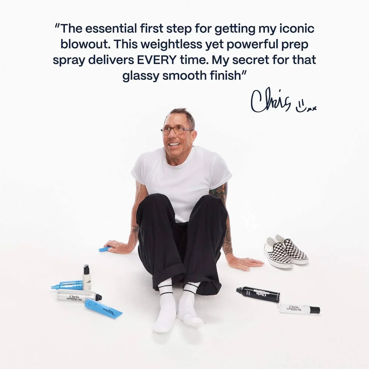 Man in white shirt and black pants sits on white background with luxe haircare products and stylish slip-on shoes, promoting smooth, glassy finish beauty essentials.