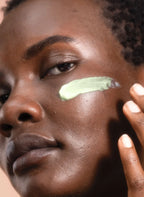 Model with glowing skin applying creamy green skincare product on cheek
