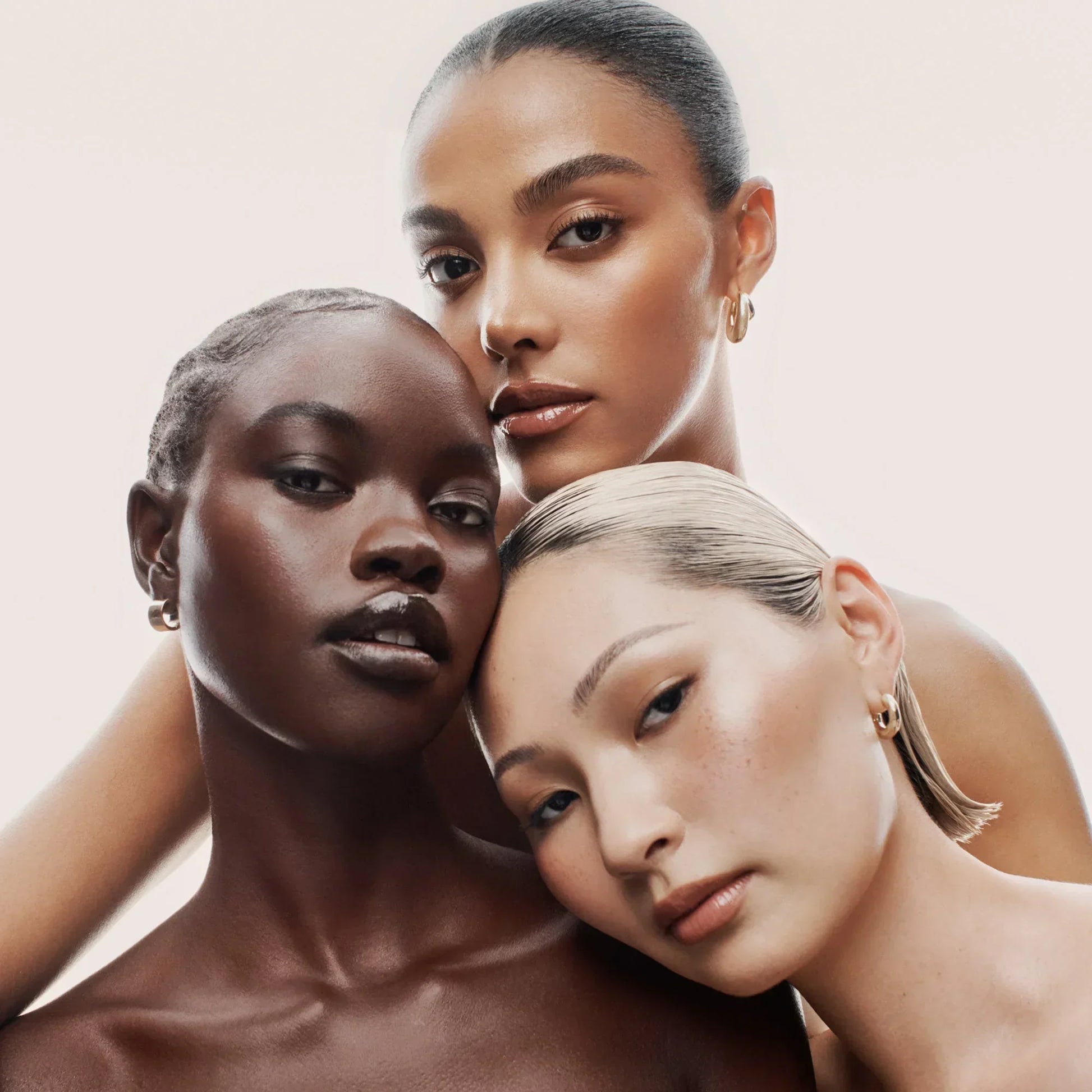 Three women with radiant, flawless skin in diverse tones, featuring dewy, luminous makeup.