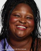 Smiling woman with braided hair, radiant skin, and red jelly tint blush on cheeks, close-up.