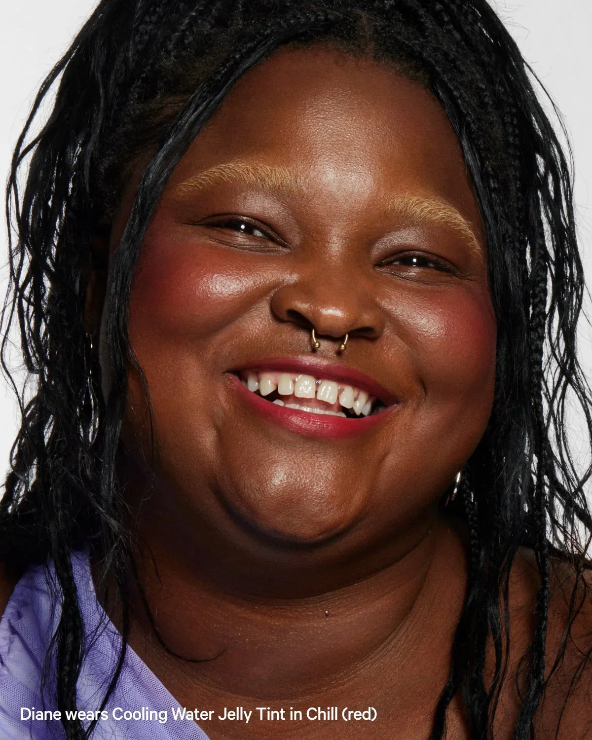 Smiling woman with braided hair, radiant skin, and red jelly tint blush on cheeks, close-up.