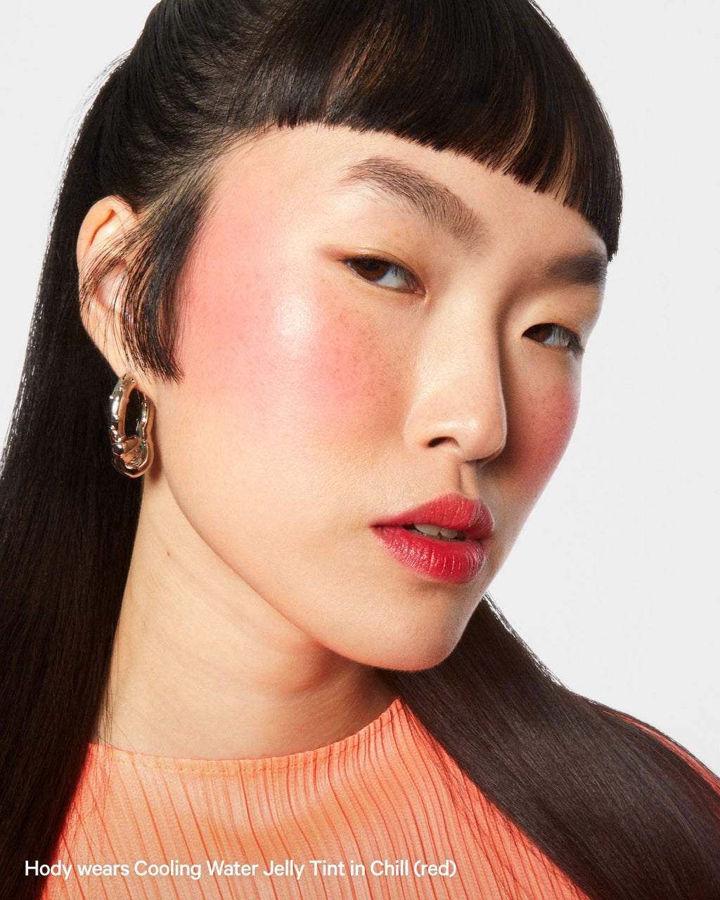 Woman with Cooling Water Jelly Tint Chill red on cheeks and lips, wearing an orange top