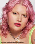 Woman with pink hair wearing berry jelly lip tint and green top, elegant necklace, studio portrait.