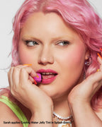 Woman with pink hair applies berry Jelly Tint lip product to lips, vibrant makeup look