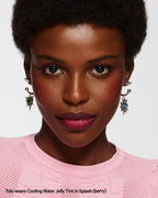 Woman wearing berry Cooling Water Jelly Tint, statement earrings, and pink top, close-up portrait.