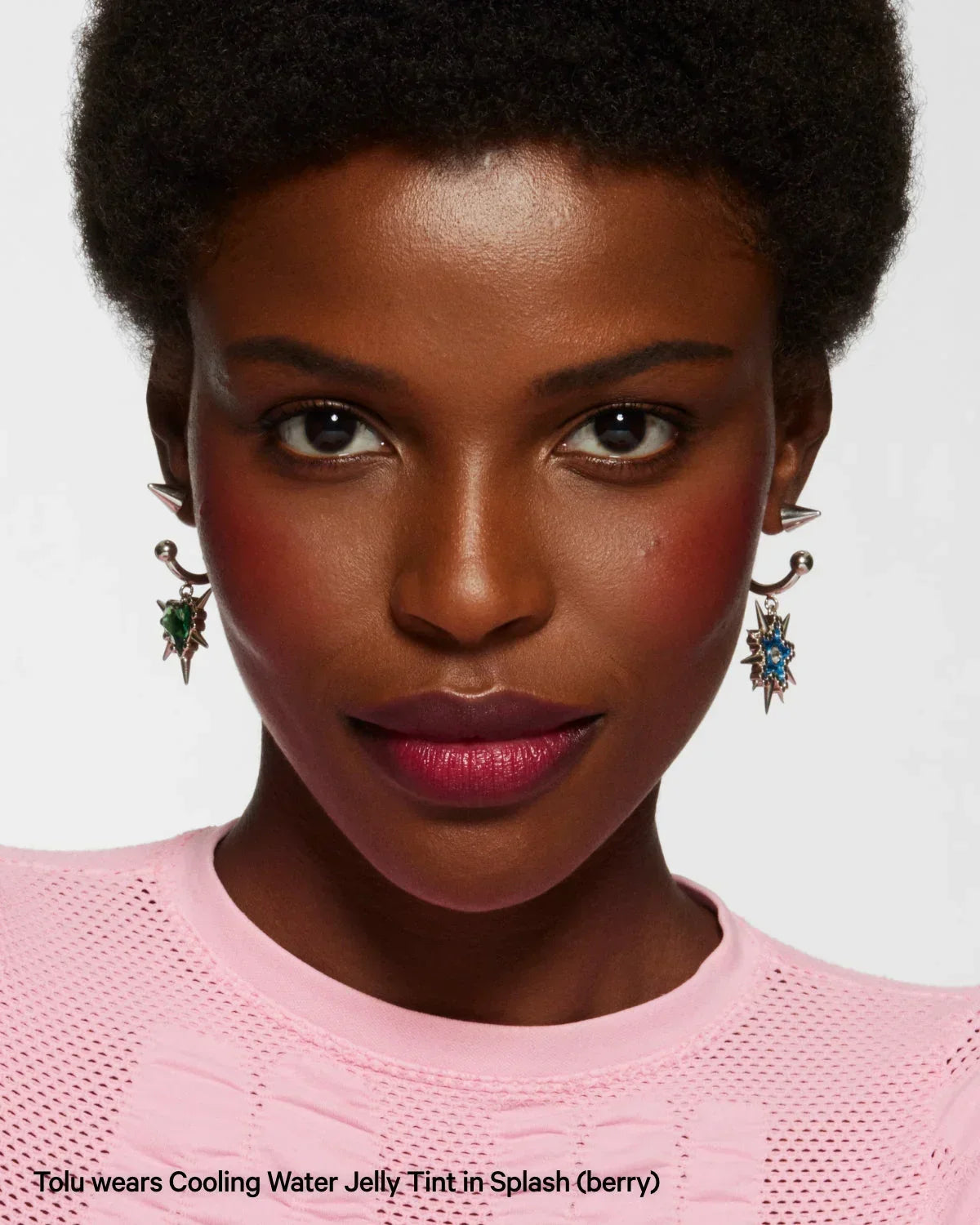 Woman wearing berry Cooling Water Jelly Tint, statement earrings, and pink top, close-up portrait.