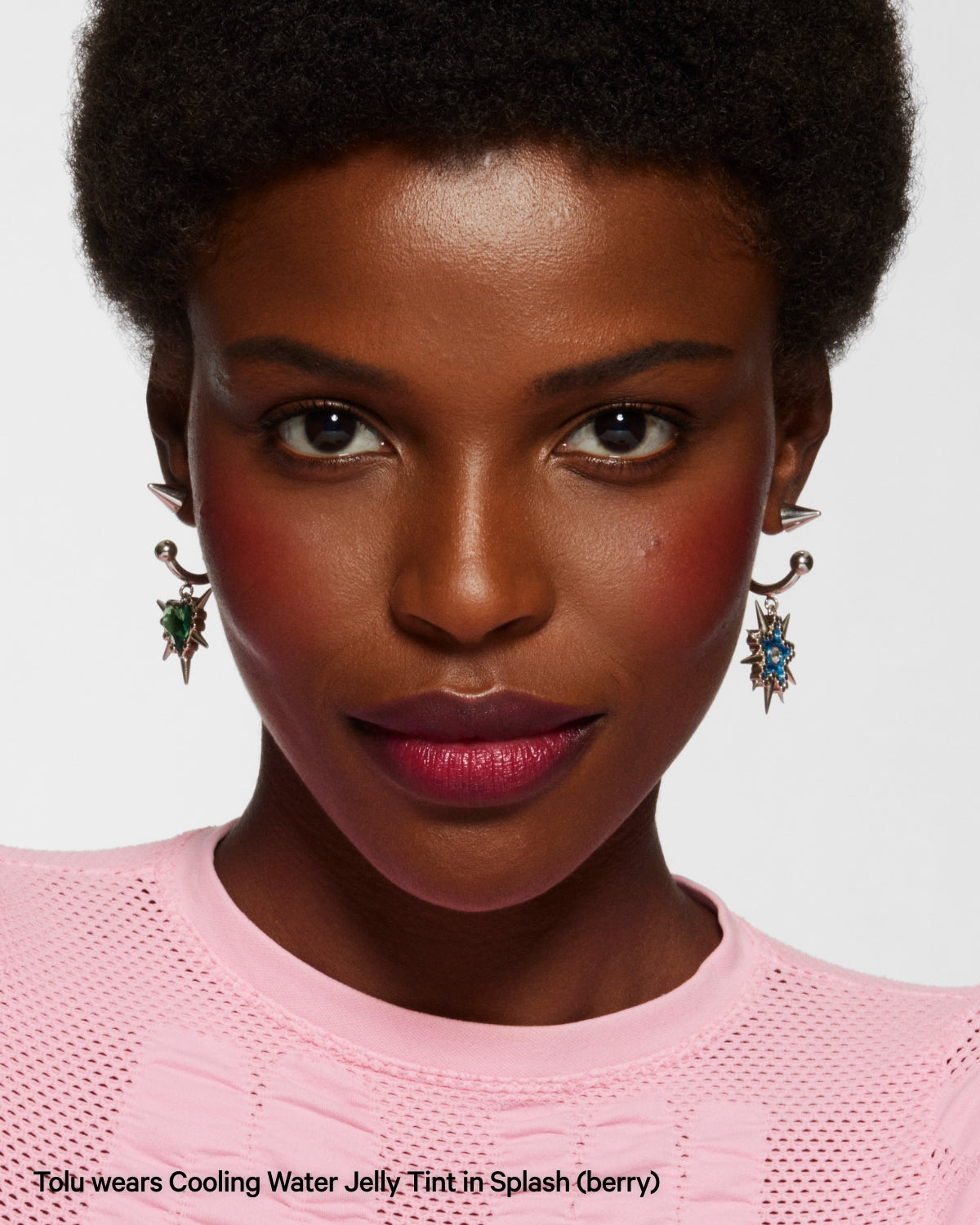 Woman wearing berry Cooling Water Jelly Tint, statement earrings, and pink top, close-up portrait.