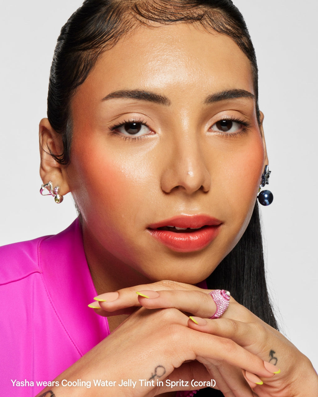 Woman with glowy coral blush, glossy lips, and vibrant pink top, close-up beauty portrait