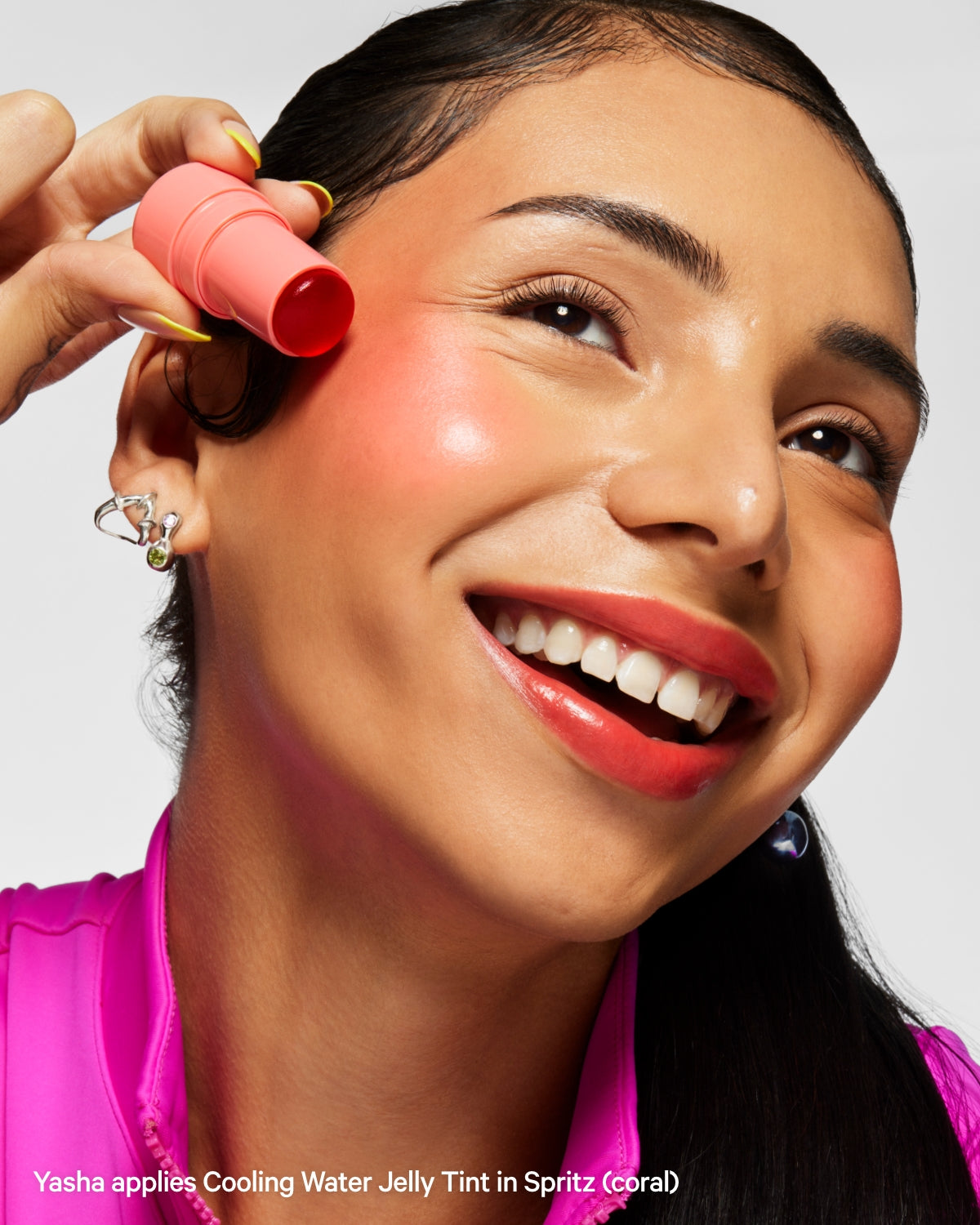 Smiling woman applying coral Cooling Water Jelly Tint to cheek, close-up beauty shot