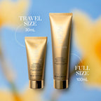 KORA Organics Turmeric Brightening & Exfoliating Scrub Mask in gold tubes, travel and full size, on a soft blue floral background.