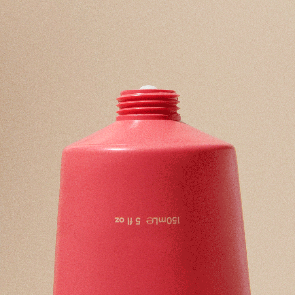 Vibrant coral tube squeezing creamy skincare on beige background, Wylde Grey beauty essentials