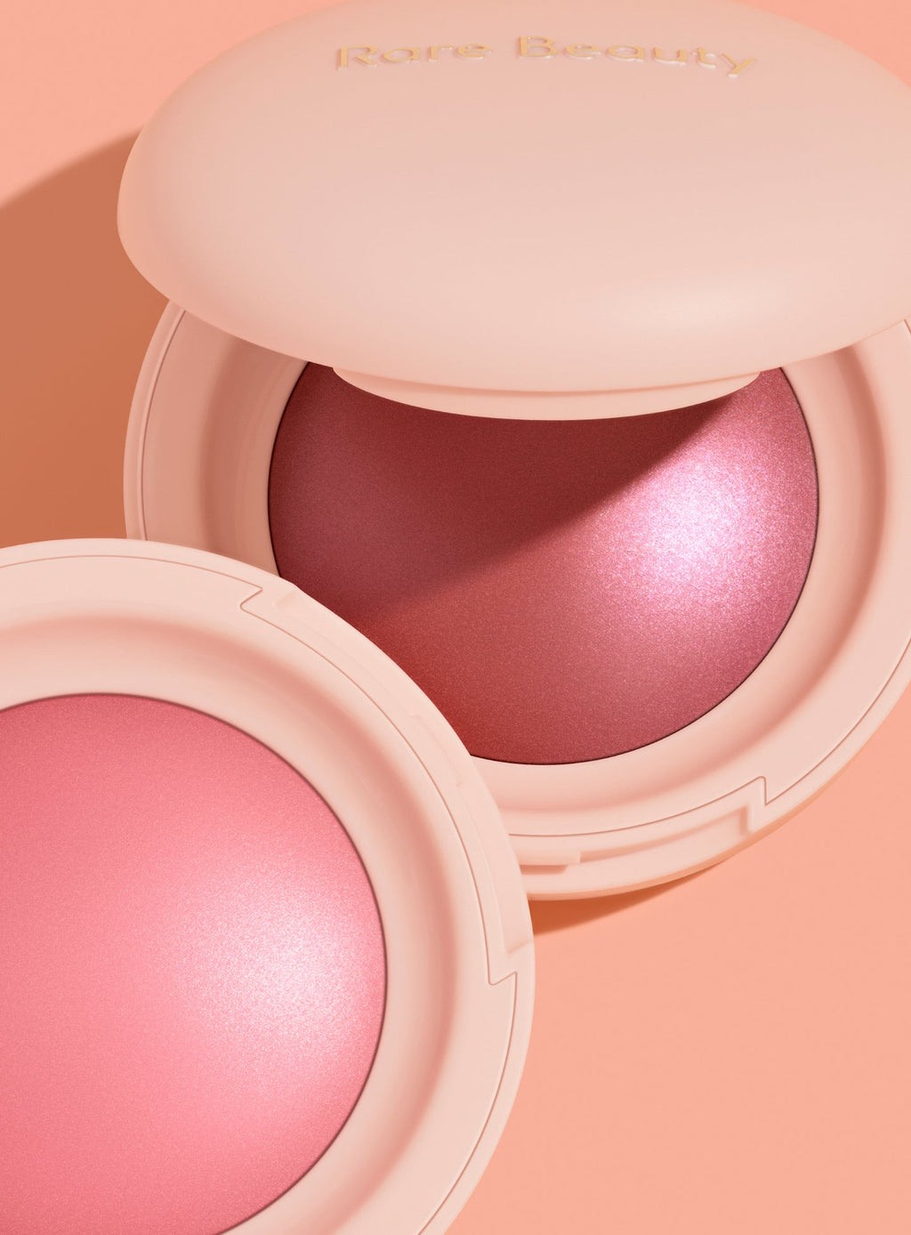 | A close-up shot of two shades of Rare Beauty's Soft Pinch Luminous Powder Blush laying open against a pink background.