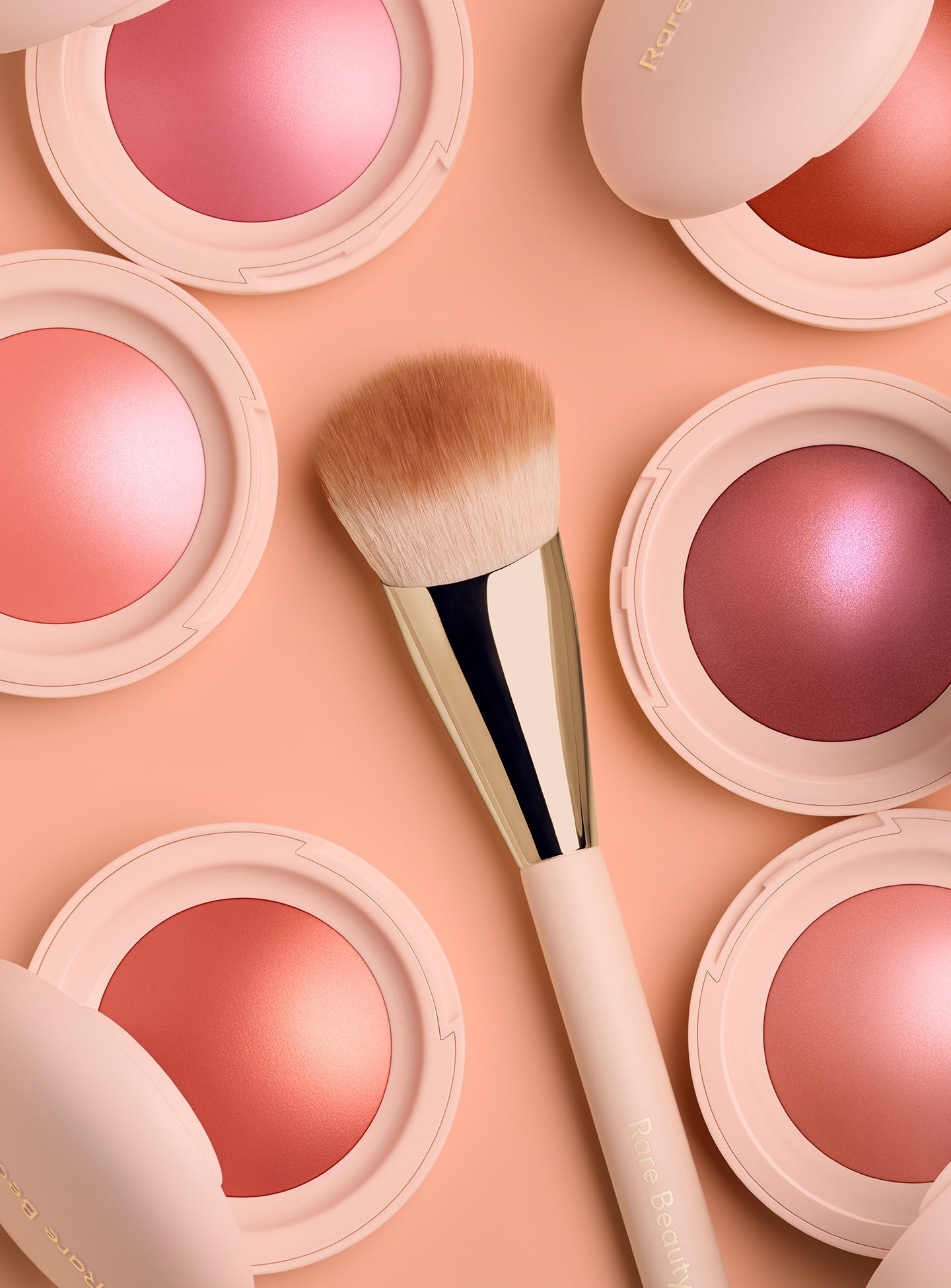 | Rare Beauty's Soft Pinch Blush Brush lies in the center of six different shades of the Soft Pinch Luminous Powder Blush.