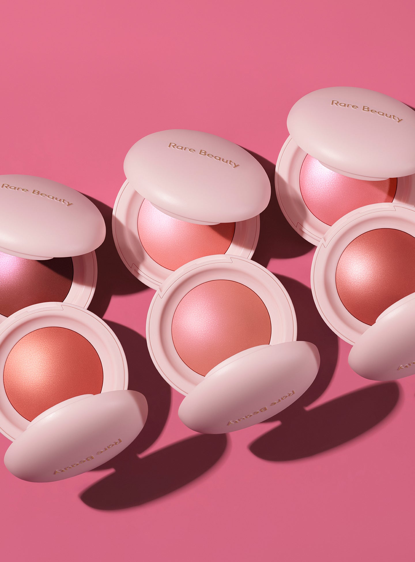 | All six shades of Rare Beauty's Soft Pinch Luminous Powder Blush lay on a pink background.