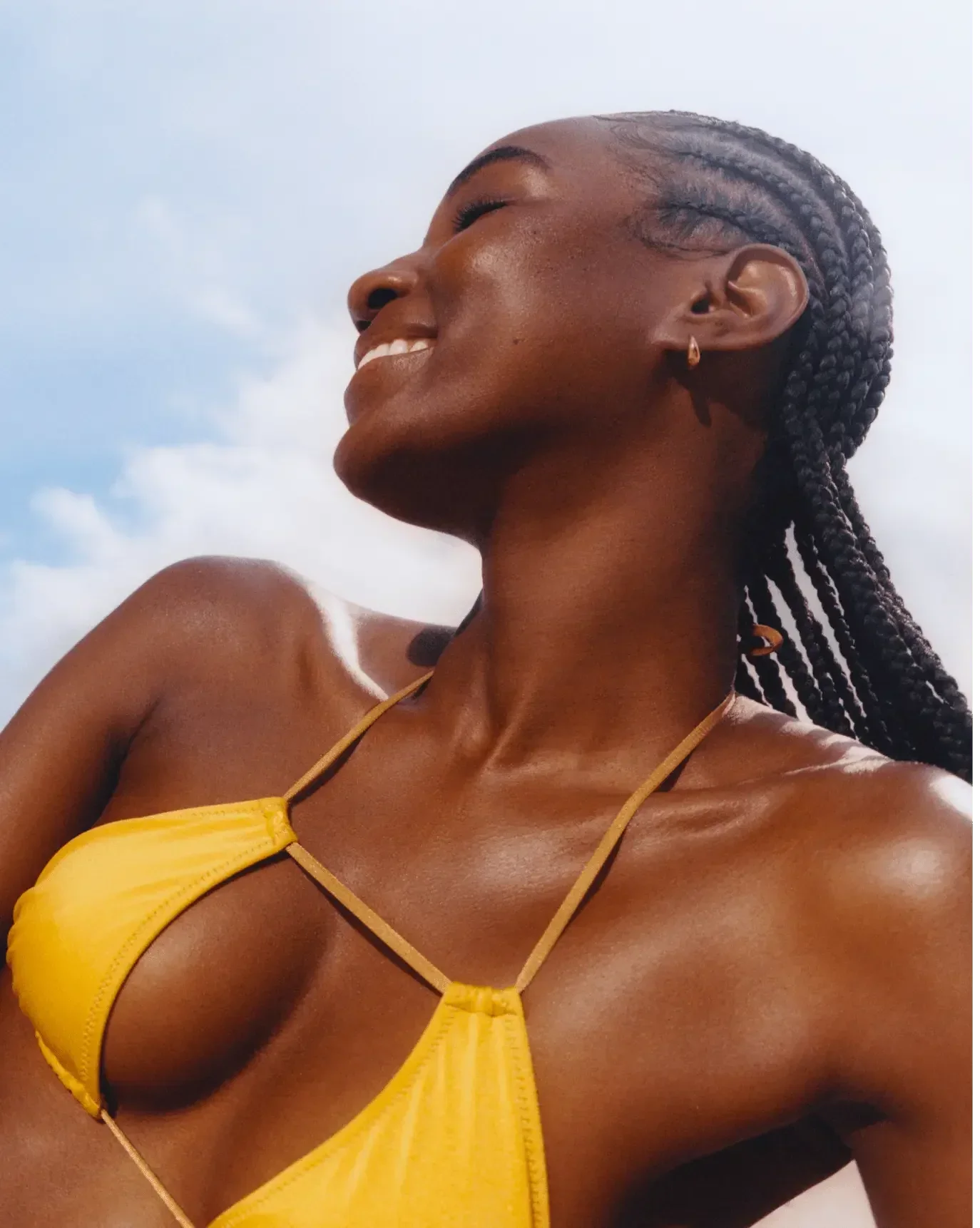 Woman with glowing, dewy skin in a yellow bikini top, smiling under natural sunlight.